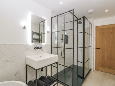 A bathroom with a glass shower enclosure sink with black fixtures and a wooden door at Tilia Barn in Wincanton
