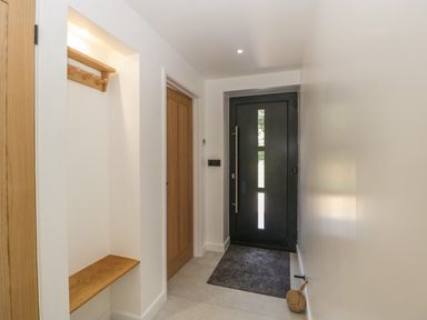 A hallway with a black front door wood bench and coat rack at Tilia Barn in Wincanton