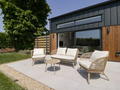 An outdoor patio with three cushioned chairs and a small round table at Tilia Barn in Wincanton