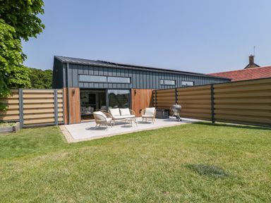 A backyard with a patio set and a barbecue grill next to a modern building at Tilia Barn in Wincanton