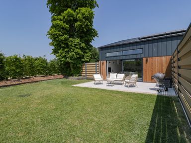 A backyard with a patio set of chairs and a table next to a modern house at Tilia Barn in Wincanton