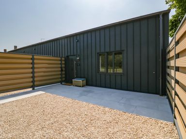 An outdoor area with a black building wall a door a window gravel ground and beige fencing at Tilia Barn in Wincanton