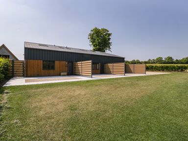 A lawn in front of a modern building with wooden and metal fencing at Tilia Barn in Wincanton
