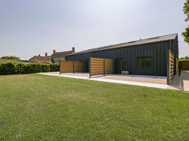 A modern building with dark siding and wooden slatted panels on a lawn at Tilia Barn in Wincanton