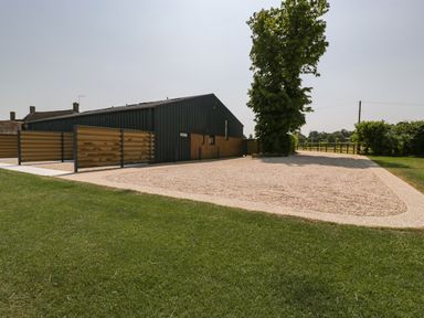 A gravel driveway next to a green building with a tree at Tilia Barn in Wincanton