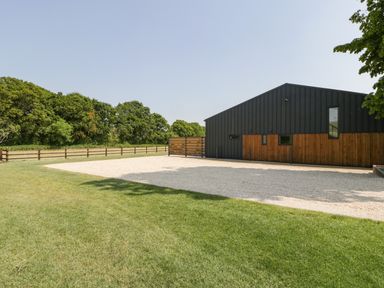 A grassy lawn and gravel area beside a black and wooden building with trees in the background at Tilia Barn in Wincanton