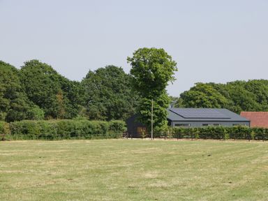 A field with grass and a metal barn with solar panels surrounded by trees at Tilia Barn in Wincanton