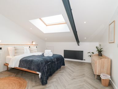 A bedroom with a bed a skylight a wooden dresser plants and a radiator at Tilia Barn in Wincanton
