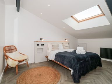 A bedroom with a bed covered with a dark blanket next to a chair and a circular rug at Tilia Barn in Wincanton