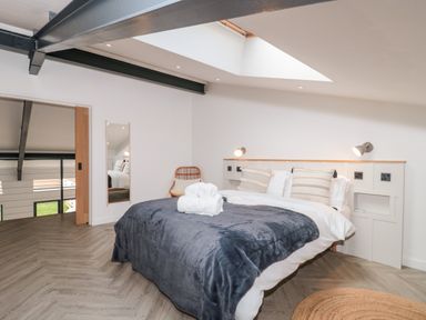 A bedroom with a double bed a dark blanket and rolled towels a wall mirror and a chair at Tilia Barn in Wincanton