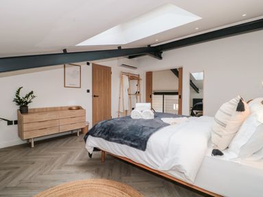 A bedroom with a bed with pillows and rolled towels a wooden dresser plant and a wooden clothes rack at Tilia Barn in Wincanton