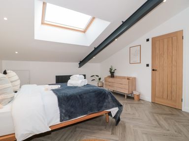 A bedroom with a bed, a wooden dresser, a wooden door, a ceiling beam, a skylight, and folded towels on the bed at Tilia Barn in Wincanton