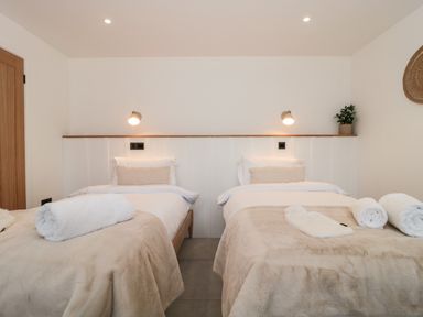 A bedroom with two single beds made with beige blankets and white towels at Tilia Barn in Wincanton