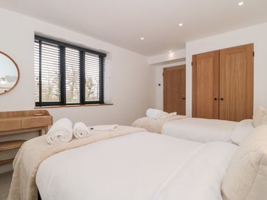 A bedroom with two beds rolled towels on each bed a wooden desk under a window with blinds and wooden doors at Tilia Barn in Wincanton