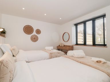 A bedroom with two beds and rolled towels on them and a wooden desk with a round mirror at Tilia Barn in Wincanton