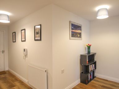 A hallway with framed pictures on the wall a small bookshelf with books and a vase of flowers at Nautical Breeze in Weymouth
