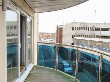 A balcony with glass and metal railing overlooking a street with buildings and parked cars at Nautical Breeze in Weymouth