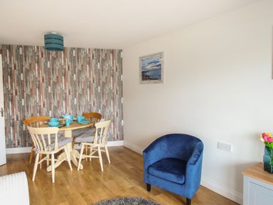 A dining area with wooden table and chairs and a blue armchair in a room at Nautical Breeze in Weymouth