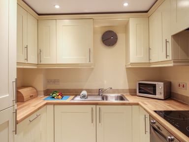 A kitchen with beige cabinets wooden countertops a sink a microwave and a clock on the wall at Nautical Breeze in Weymouth