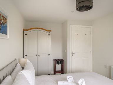 A bedroom with a bed white bedding a wardrobe a door a lamp and a luggage rack at Nautical Breeze in Weymouth