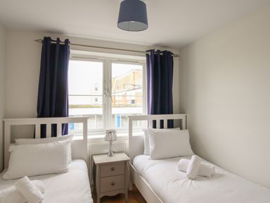 A bedroom with two single beds separated by a nightstand with a lamp at Nautical Breeze in Weymouth