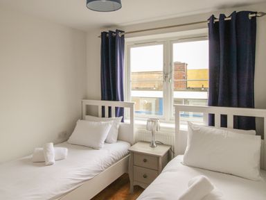 A bedroom with two single beds a small bedside table and a window with dark curtains at Nautical Breeze in Weymouth