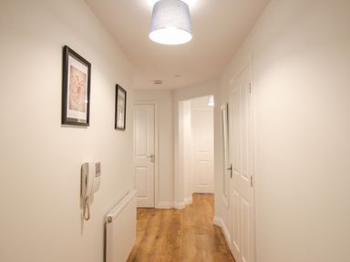 A hallway with wooden floor white walls two framed pictures and closed doors at Nautical Breeze in Weymouth