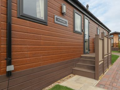 Exterior view of a building with wooden siding steps leading to a door and windows at Sea Holly Lodge in Runswick Bay