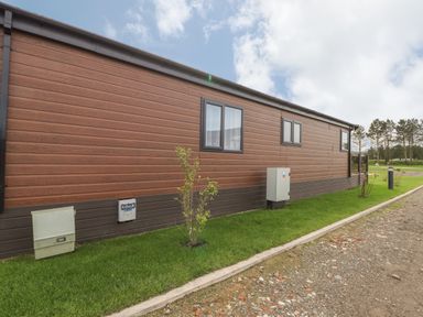 The side view of a single story brown and dark brown building with windows small bushes on a grass strip and a gravel path