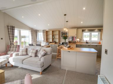An open plan living room and kitchen with plaid cushions and curtains at Sea Holly Lodge in Runswick Bay