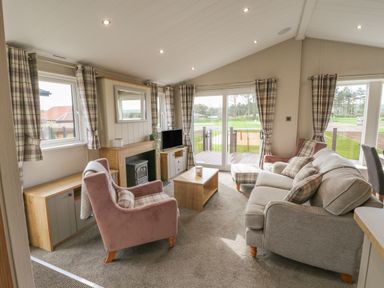 A living room with sofa armchairs coffee table and TV at Sea Holly Lodge in Runswick Bay