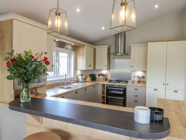A kitchen with cabinets a stove a sink flowers in a vase and two cups on a counter at Sea Holly Lodge in Runswick Bay