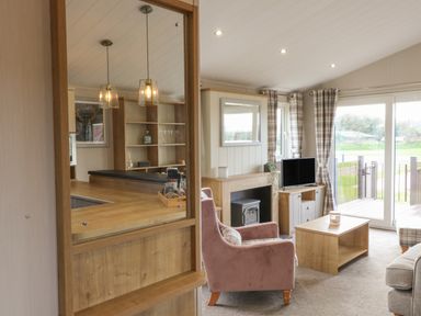 A living room with a pink armchair a television a coffee table and large windows at Sea Holly Lodge in Runswick Bay