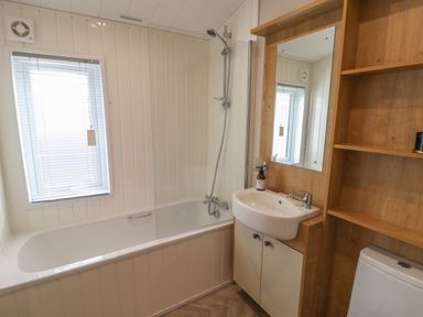 A bathroom with a bathtub a shower sink and wooden shelving at Sea Holly Lodge in Runswick Bay