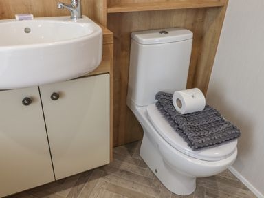 A bathroom with a white sink, a cabinet, a toilet with gray towels and a roll of toilet paper on the lid at Sea Holly Lodge in Runswick Bay