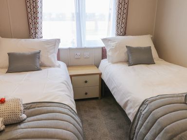 A bedroom with two single beds separated by a wooden nightstand with drawers at Sea Holly Lodge in Runswick Bay