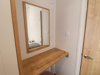 A wooden wall-mounted table with a wooden framed mirror above it and a door with a metal handle nearby at Sea Holly Lodge in Runswick Bay