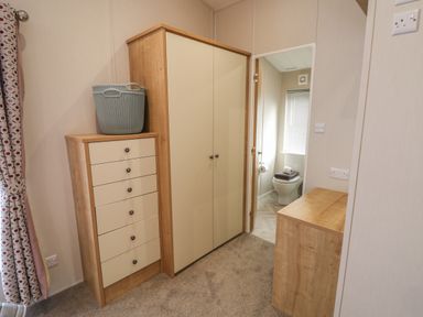 A room with a chest of drawers a wardrobe a wooden cabinet and a bathroom visible through an open door at Sea Holly Lodge in Runswick Bay