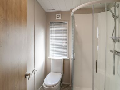 A bathroom with a toilet a shower enclosure and a window with blinds at Sea Holly Lodge in Runswick Bay