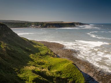 A coastal view with green cliffs and a rocky shoreline at Sea Holly Lodge in Runswick Bay