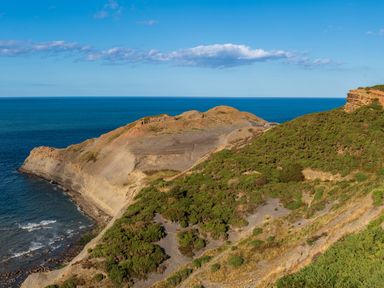 A coastal cliff with green vegetation and rocky formations beside the blue sea at Sea Holly Lodge in Runswick Bay