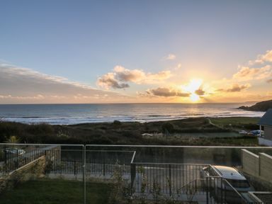 A view of the ocean with waves and a sunset seen from behind a balcony with railings and a parked car at Sea Sands in Praa Sands