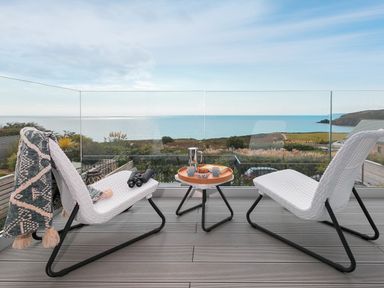 A balcony with two white chairs and a table with tea set overlooking the sea at Sea Sands in Praa Sands