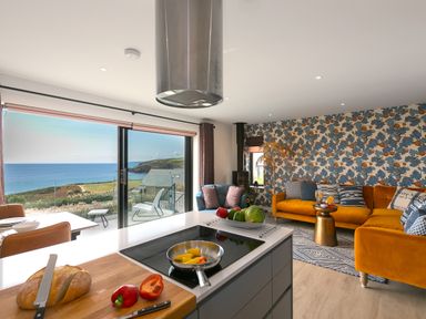 An open kitchen and living room with a cooking island cutting board with bread and peppers and a sea view at Sea Sands in Praa Sands