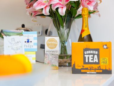 A kitchen counter with a bottle of Mionetto prosecco Cornish tea fudge biscuits and a vase with pink lilies at Sea Sands in Praa Sands