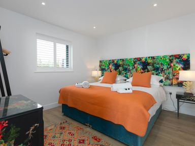 A bedroom with a large bed with orange bedding and colorful headboard at Sea Sands in Praa Sands