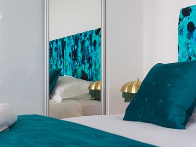 A bedroom with a teal headboard teal pillows white bedding and a brass lamp at Sea Sands in Praa Sands