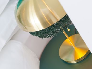 A brass table lamp with green fringes on a round green bedside table next to a white pillow at Sea Sands in Praa Sands