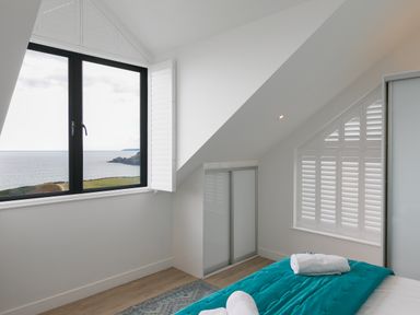 A bedroom with a window overlooking the sea and cliffs at Sea Sands in Praa Sands