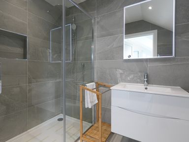 A bathroom with a glass shower enclosure a wooden towel rack and a white sink with a mirror at Sea Sands in Praa Sands